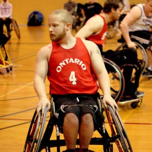 A front-facing photo of athlete Eric Voss in his basketball wheelchair wearing a red Ontario jersey #4