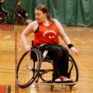 a girl wearing a red Ontario jersey in a basketball wheelchair pivoting to the left during a game